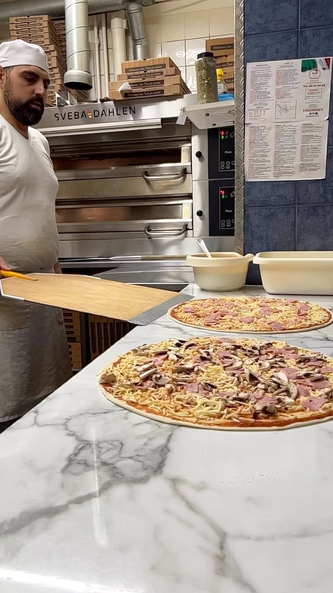 Pizzabagare med pizzor i köket